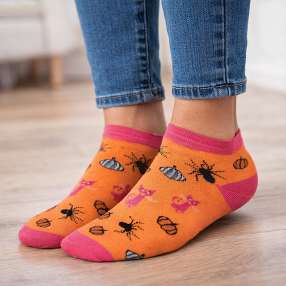 Orange Ankle Halloween socks with insect patterns and pink toes worn with blue jeans on a wooden floor.