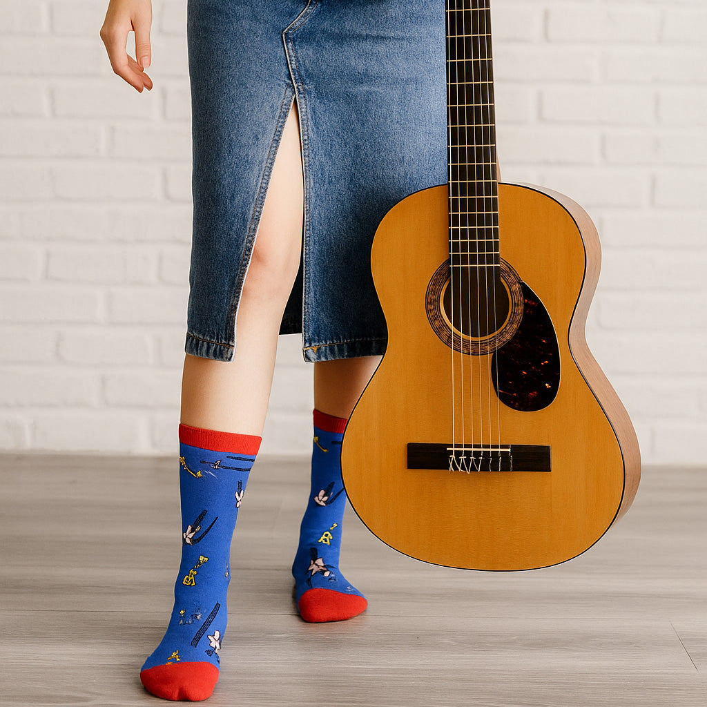 Person wearing blue socks with red toes holding an acoustic guitar against a white brick wall.